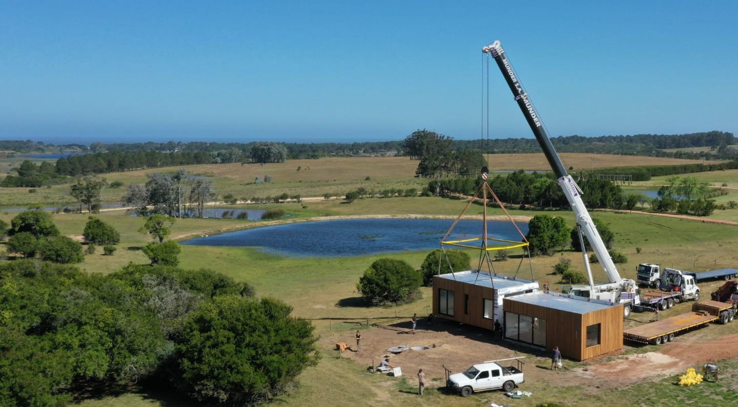 Grúa colocando los módulos de una casa de Fábrica de Casas junto a una laguna